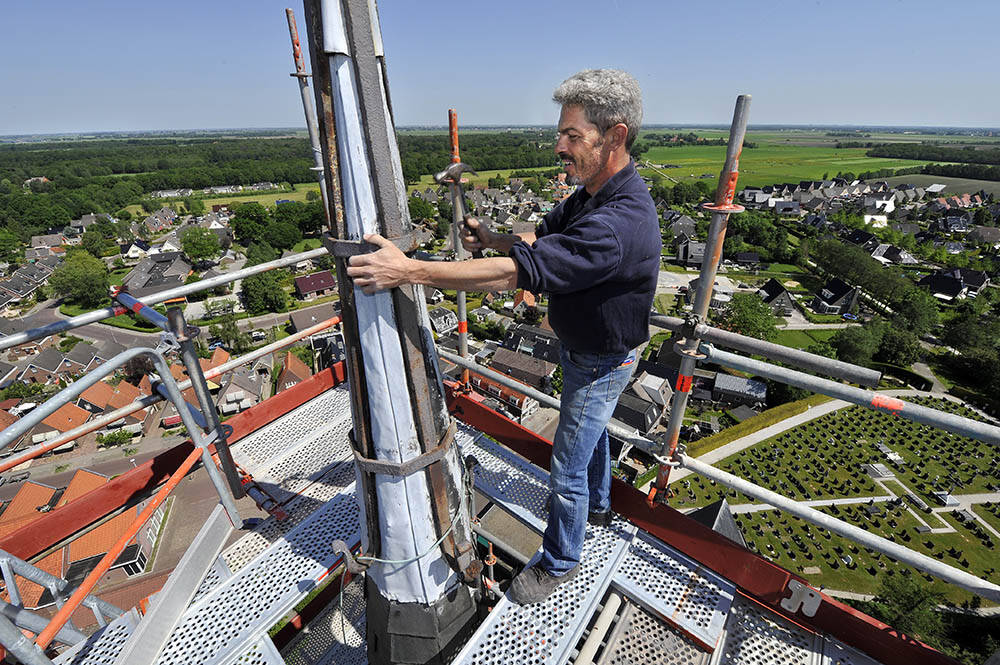 Het ijzerwerk van het torenkruis van de rooms-katholieke kerk in Sint Nicolaasga zal op delen moeten worden vervangen. Op 61 meter hoogte ziet Marc Fuchs van leidekkersbedrijf J. Zijlstra uit Heerenveen de mankementen pas goed. Hij is druk bezig met het vervangen van de leien van de ranke spits en de traptoren, die er tegenaan is gebouwd.  Een van de zijbeuken van de neogotische kruisbasiliek, die in 1887 door architect Jan Doedes van der Weide is gebouwd, krijgt ook nieuwe leien. De planken van het houten dakdek verkeren in relatief nog prima staat. Drie spijkers op elke kant en – afhankelijk van de lengte van de planken – ook in het midden zorgen ervoor dat ze weer vast op hun plek zitten.  De werkzaamheden  maken onderdeel van een zesjarig onderhoudsplan. In deze rond worden de balustrade van de torenspits opgeknapt. Met speciale reparatiemortel maakt Repstone in Ameide de natuurstenen pinakels weer in orde. Afhankelijk van de staat worden ook nieuwe natuurstenen afdekkers aangebracht. Alle loodaansluitingen van het rijksmonument en de dakkajuiten worden ook nagekeken.