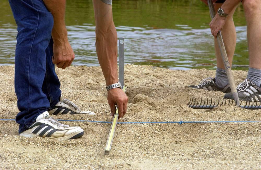 Leden van de technische commissie van de fierljeppersbond doen hun werk nadat een deelnemer zijn sprong heeft gemaakt.  Ze meten de afstand precies op, noteren die en zetten de gesprongen aantal meters op het scorebord.