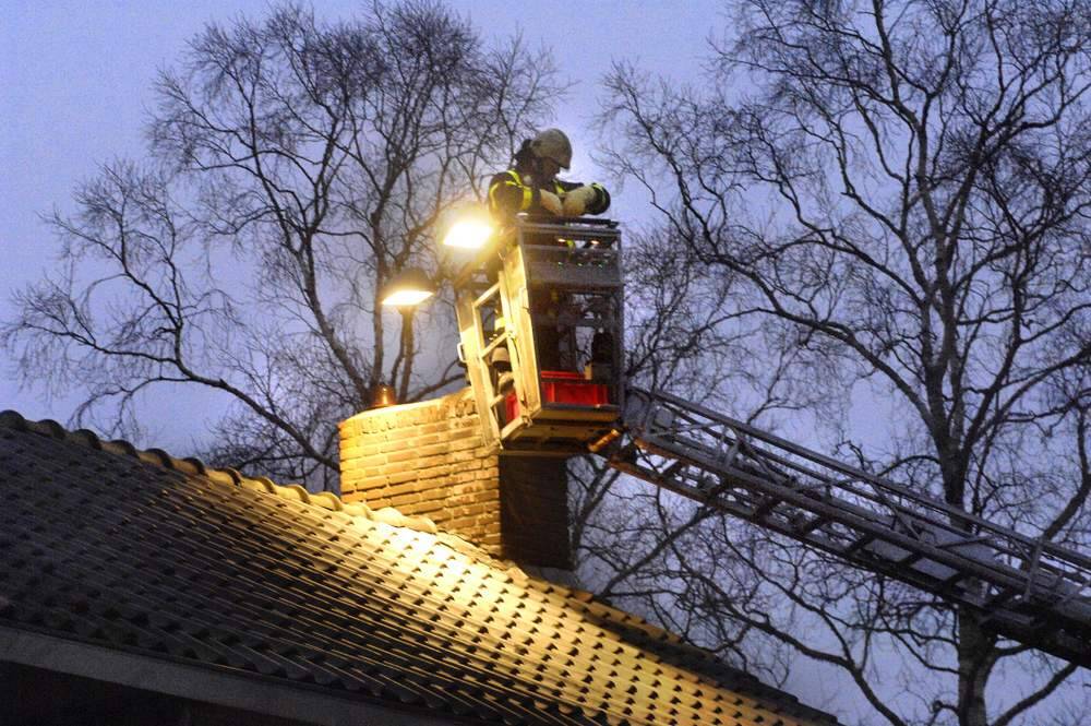 Een brandweerman wacht geduldig bij een schoorsteen van een huis aan de Nieuwstraat in Heerenveen. Hij verleent assistentie bij een schoorsteenbrand, die door zijn collega's in het huis zelf wordt onderzocht. Andere collega's halen intussen een vlaggenmast naar beneden, die precies in de weg van de ladderwagen stond. Daarna kon voor de brandweerman in het bakje van de hoogwerker het echte werk beginnen.